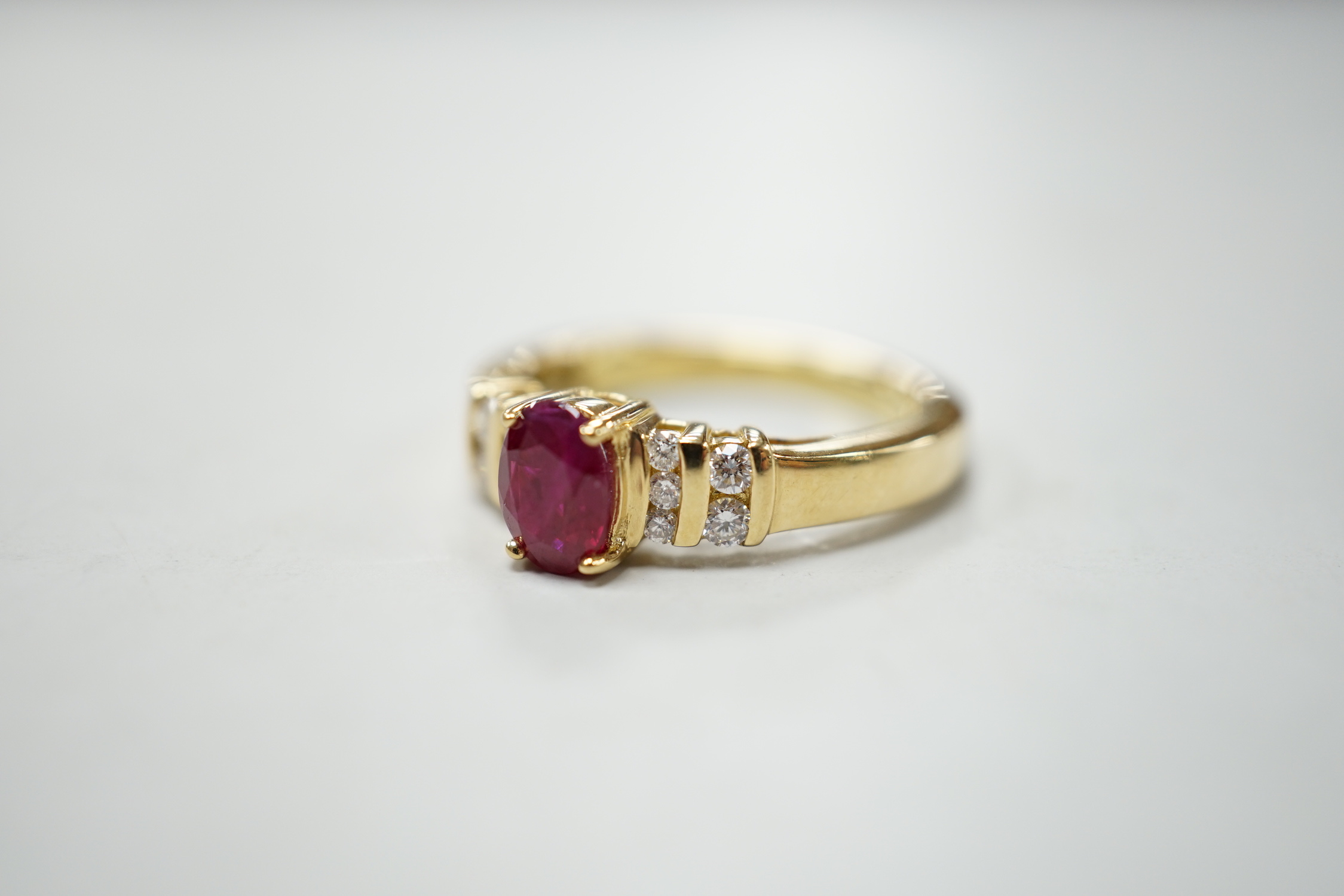 A modern yellow metal and single stone oval cut ruby set dress ring, with ten stone diamond chip set shoulders, size M, gross weight 5.7 grams.